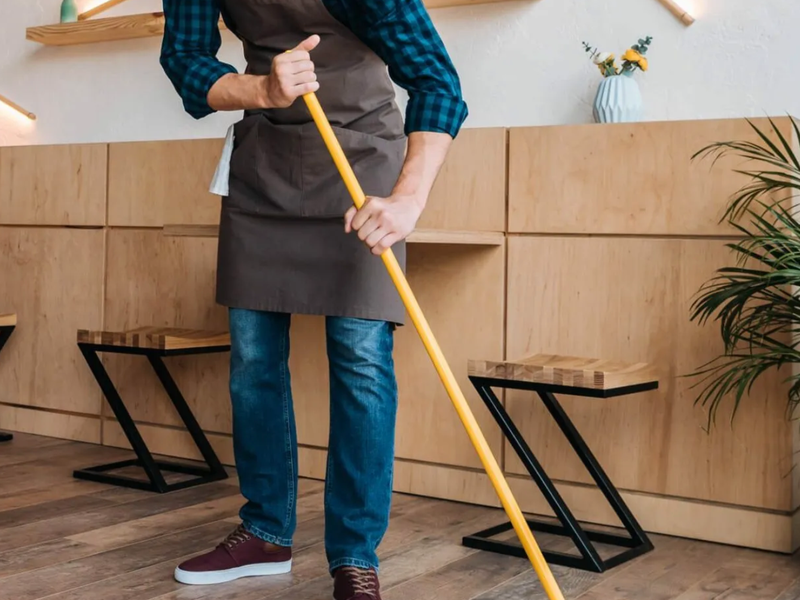 Worker sweeping wood floor in a cafe